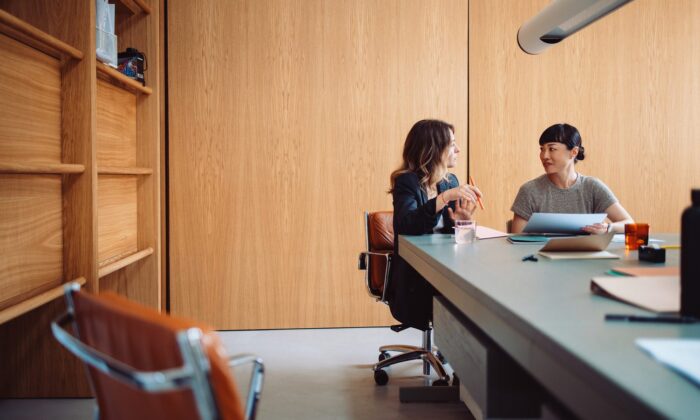 Two businesswomen engaged in a discussion at a modern office table. They are collaborating on a project with documents and laptops.