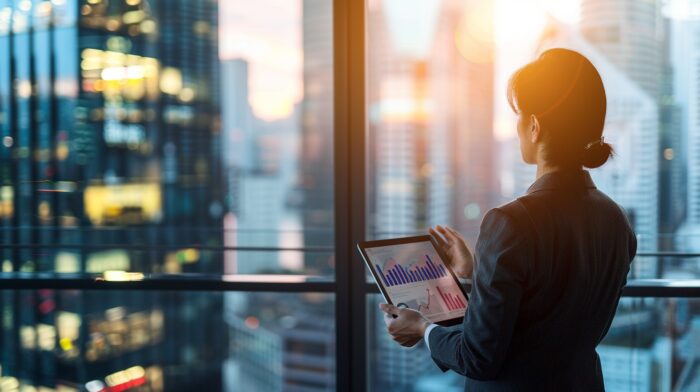 women on iPad looking at stocks near city window
