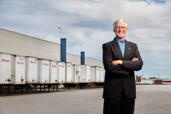 Image of a man wearing glasses standing in front of a row of container trucks