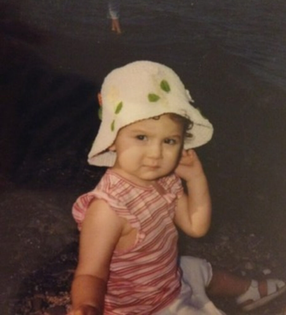 Toddler wearing a white sun hat and striped pink shirt.
