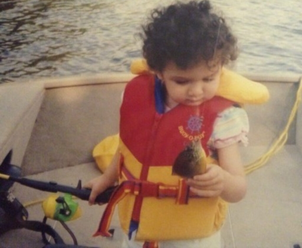 Child wearing a life jacket while holding a small fish on a boat.