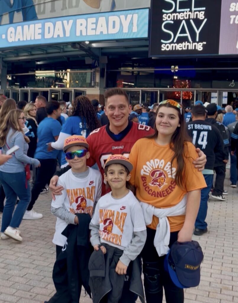 Family posing in Tampa Bay Buccaneers apparel outside a football stadium.