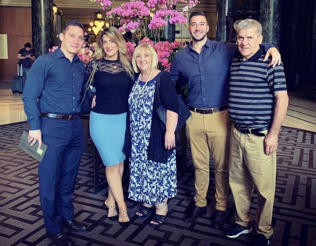 Family of five posing together in front of a display of pink orchids.
