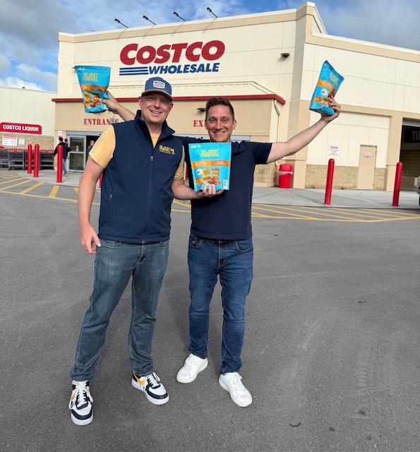 Two men holding bags of Awake snacks outside a Costco store.
